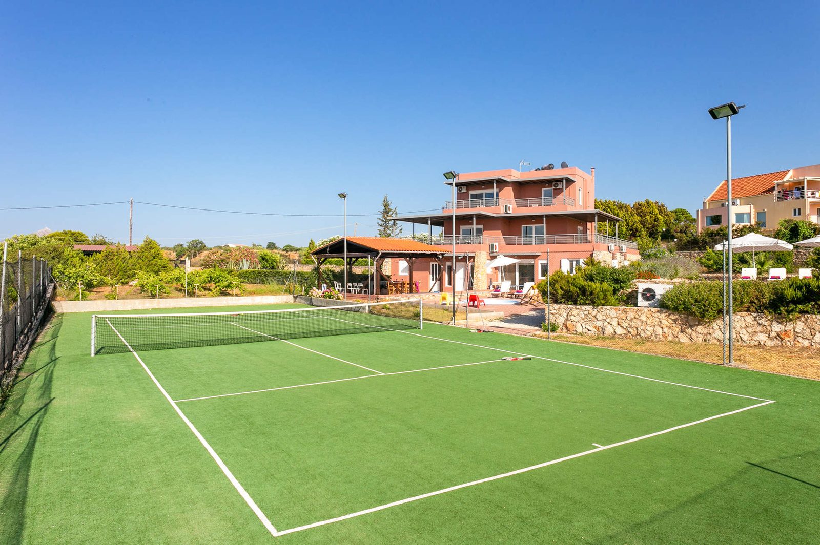 The private tennis court at Horizon Villa Kampani, with the villa and its shaded pergola behind